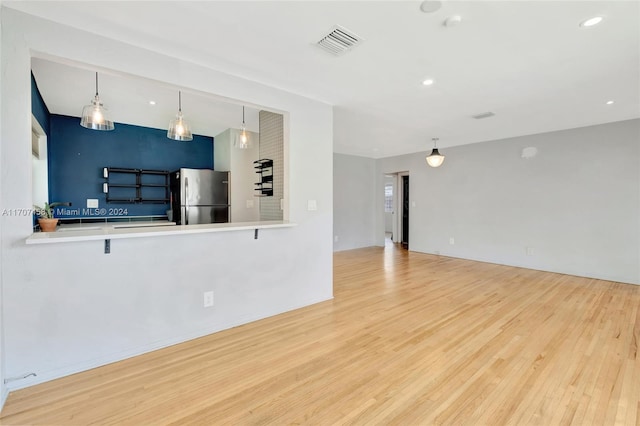 kitchen featuring kitchen peninsula, stainless steel fridge, light hardwood / wood-style flooring, and pendant lighting