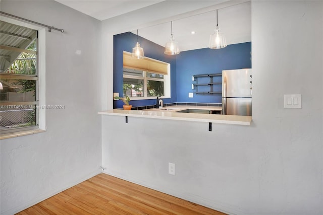 kitchen featuring hardwood / wood-style floors, a healthy amount of sunlight, hanging light fixtures, and stainless steel refrigerator