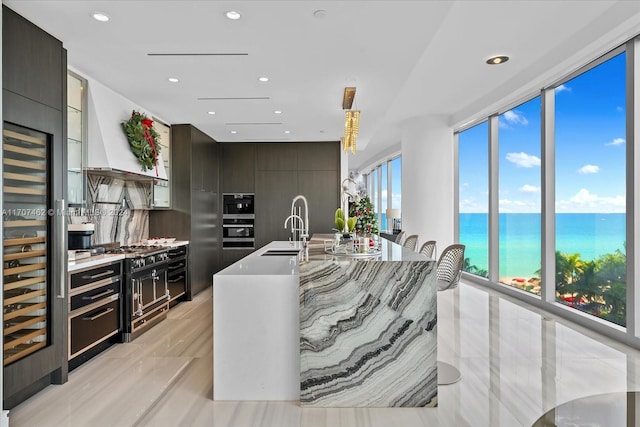 kitchen with a water view, sink, an island with sink, tasteful backsplash, and dark brown cabinetry