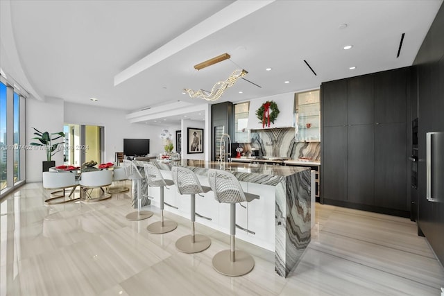 kitchen featuring light stone countertops, backsplash, sink, a large island with sink, and hanging light fixtures