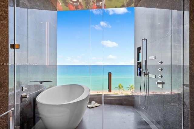 bathroom featuring a bath, a water view, tile patterned floors, and tile walls