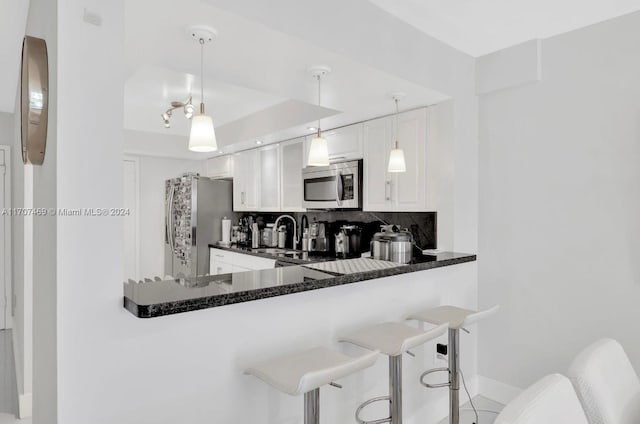 kitchen with decorative backsplash, appliances with stainless steel finishes, kitchen peninsula, decorative light fixtures, and white cabinetry