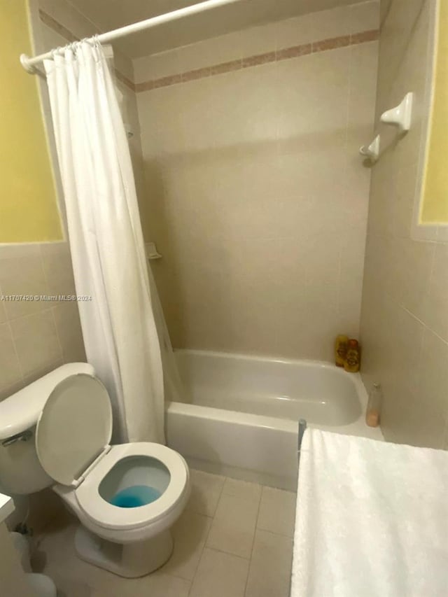 bathroom with tile patterned floors, shower / bath combination with curtain, toilet, and tile walls