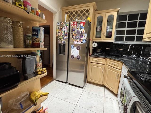 kitchen with backsplash, dark stone counters, stainless steel refrigerator with ice dispenser, light tile patterned floors, and range