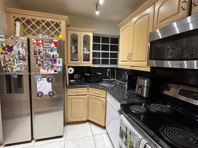 kitchen featuring decorative backsplash, appliances with stainless steel finishes, dark stone counters, sink, and light tile patterned flooring