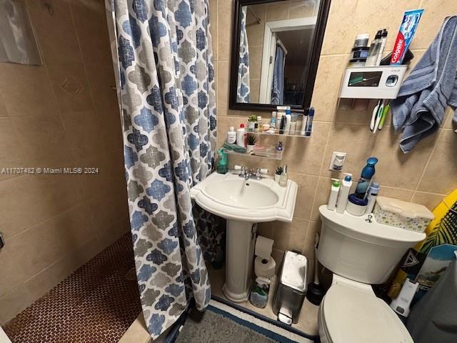 bathroom with toilet, tile walls, and a shower with shower curtain