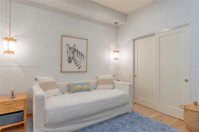 bedroom featuring light wood-style flooring, wallpapered walls, and a closet