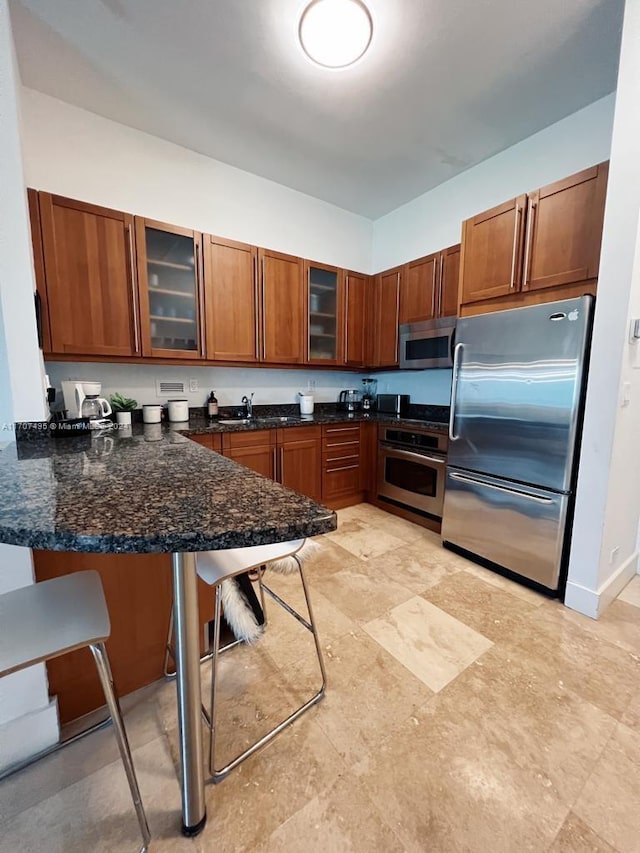 kitchen with kitchen peninsula, appliances with stainless steel finishes, a breakfast bar, sink, and dark stone countertops