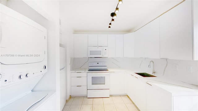 kitchen with white appliances, track lighting, white cabinets, sink, and stacked washer and dryer