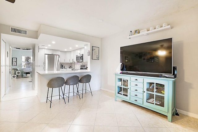 kitchen featuring kitchen peninsula, a kitchen breakfast bar, tasteful backsplash, stainless steel appliances, and white cabinetry