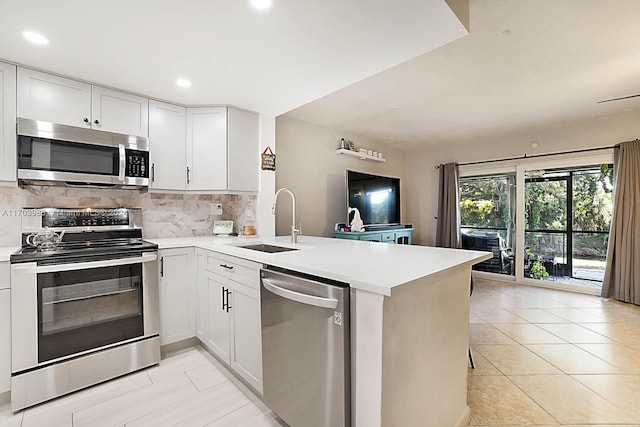 kitchen featuring backsplash, white cabinets, sink, kitchen peninsula, and stainless steel appliances