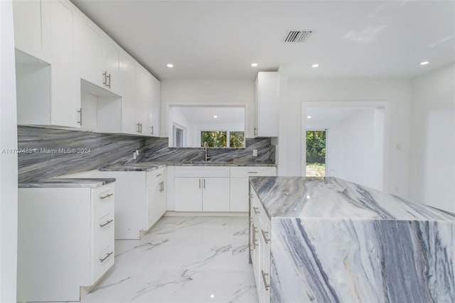 kitchen featuring stone countertops, sink, white cabinetry, and backsplash