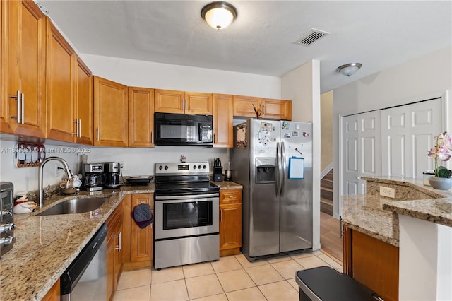 kitchen with light stone counters, stainless steel appliances, a sink, visible vents, and brown cabinetry