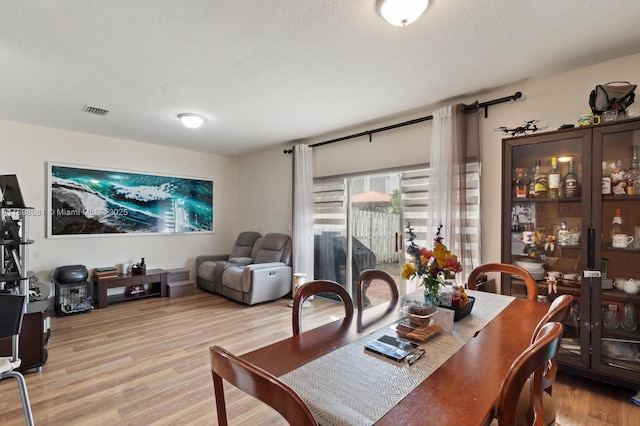 dining space featuring a textured ceiling, light wood-style flooring, and visible vents