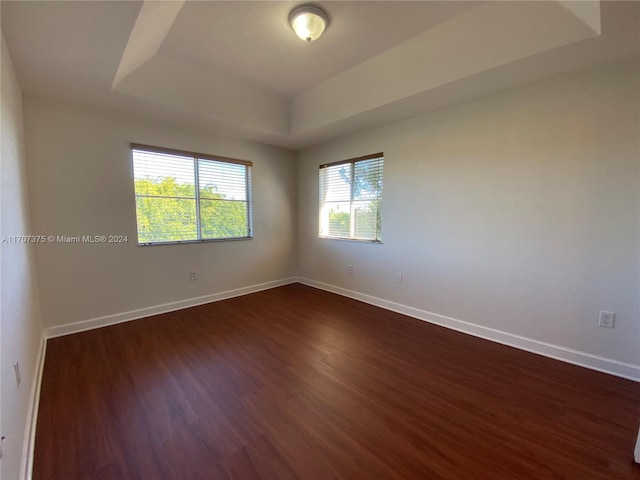 empty room with a tray ceiling and dark wood-type flooring