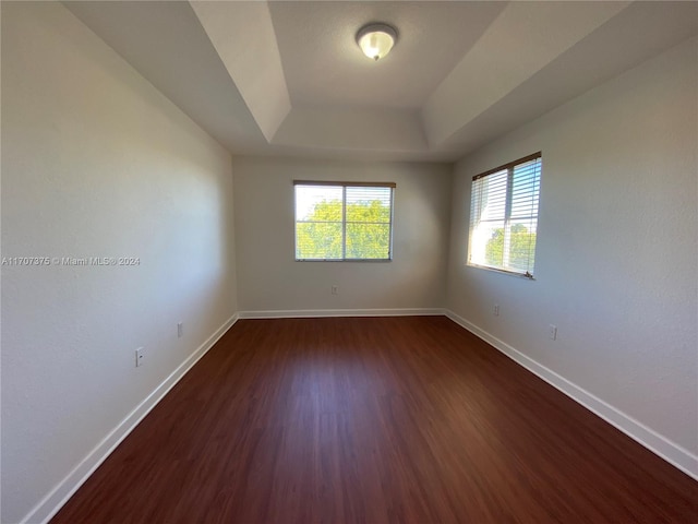 unfurnished room featuring a tray ceiling and dark hardwood / wood-style flooring