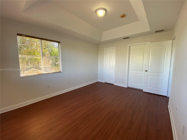 unfurnished bedroom featuring a raised ceiling and dark hardwood / wood-style flooring