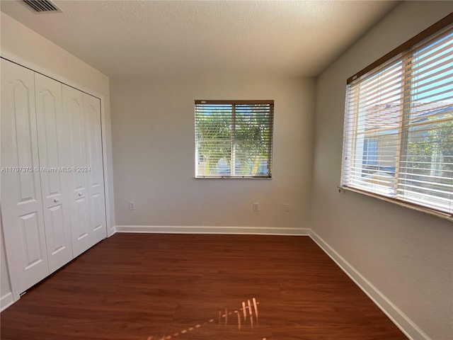 unfurnished bedroom with a closet, dark hardwood / wood-style floors, and multiple windows