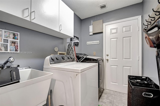 laundry area with cabinets, sink, light tile patterned floors, a textured ceiling, and washing machine and clothes dryer