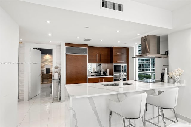 kitchen featuring kitchen peninsula, a kitchen bar, extractor fan, light tile patterned floors, and built in appliances