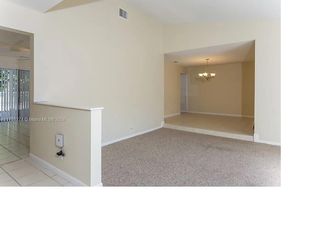 unfurnished room with ceiling fan with notable chandelier, light colored carpet, and vaulted ceiling