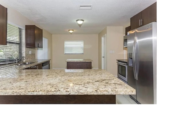 kitchen featuring sink, stainless steel appliances, kitchen peninsula, a textured ceiling, and dark brown cabinets