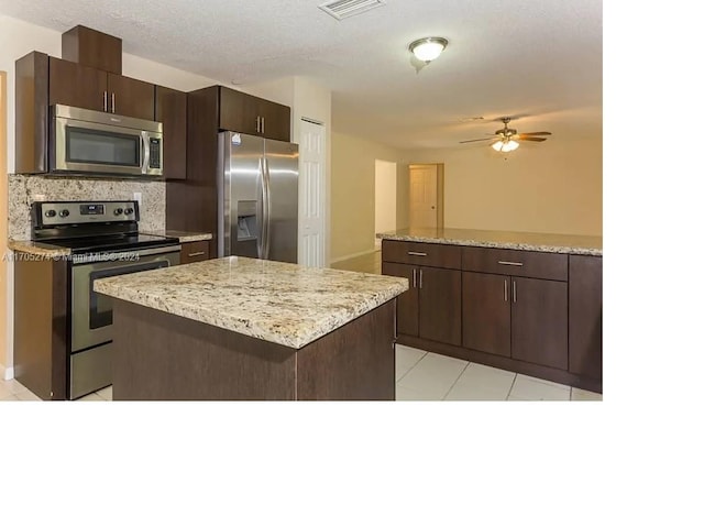 kitchen featuring decorative backsplash, appliances with stainless steel finishes, dark brown cabinets, ceiling fan, and a center island