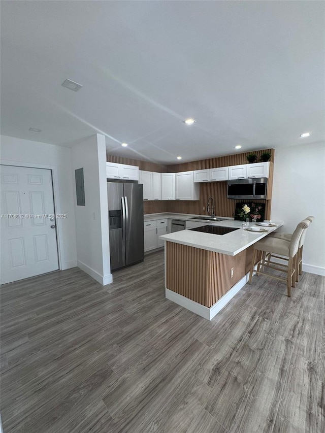 kitchen with white cabinetry, sink, a kitchen bar, hardwood / wood-style flooring, and stainless steel appliances