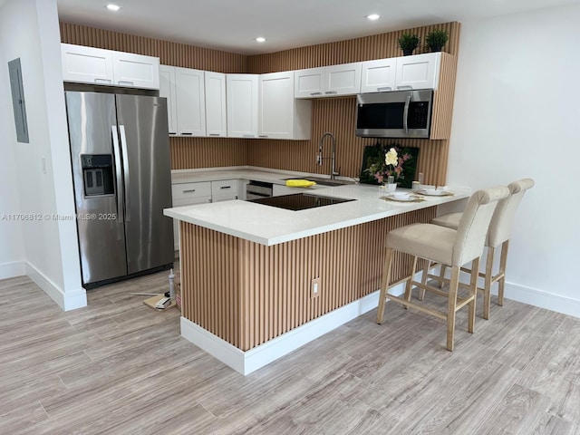 kitchen featuring a breakfast bar, sink, kitchen peninsula, stainless steel appliances, and white cabinets