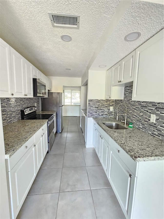 kitchen with appliances with stainless steel finishes, sink, white cabinets, light tile patterned floors, and light stone countertops