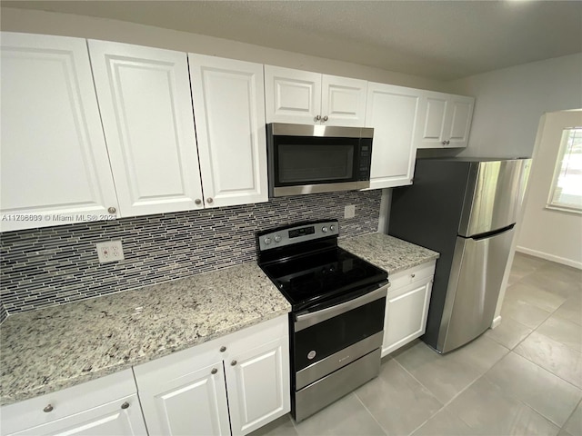 kitchen with tasteful backsplash, white cabinets, stainless steel appliances, and light tile patterned floors