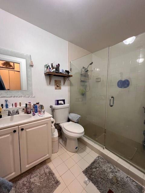 bathroom with toilet, vanity, a shower with door, and tile patterned flooring