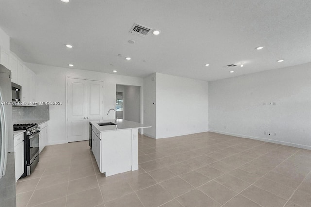 kitchen with white cabinets, appliances with stainless steel finishes, a kitchen island with sink, and sink