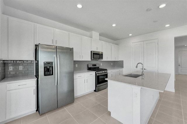 kitchen with sink, an island with sink, light stone counters, white cabinetry, and stainless steel appliances