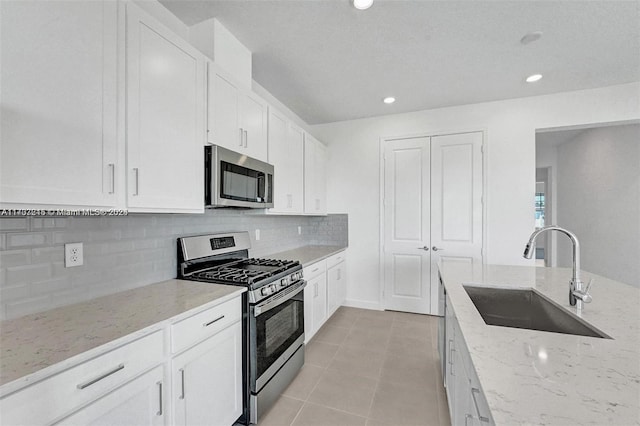 kitchen featuring sink, light tile patterned floors, appliances with stainless steel finishes, light stone counters, and white cabinetry