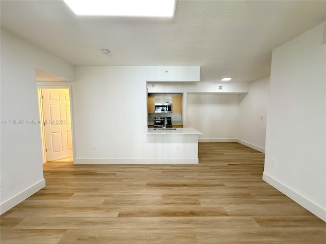 unfurnished living room featuring light wood-style floors, a sink, a textured ceiling, and baseboards