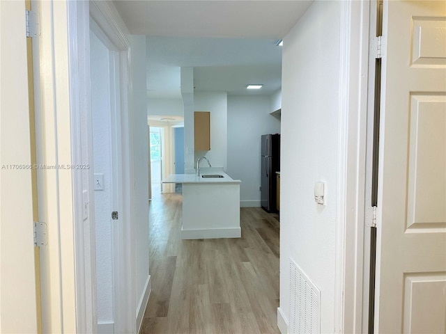hallway featuring baseboards, visible vents, light wood-type flooring, and a sink