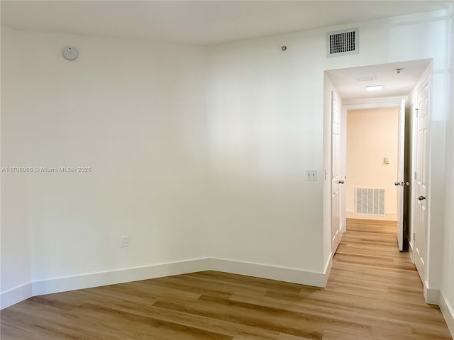 corridor with light wood-style floors, visible vents, and baseboards