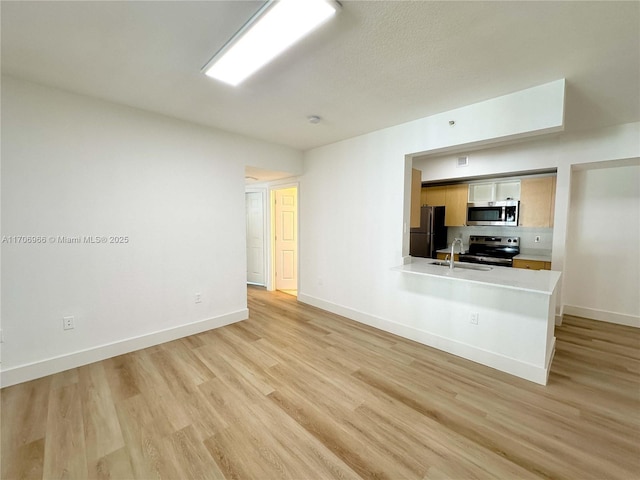 unfurnished living room with a sink, baseboards, and light wood-type flooring