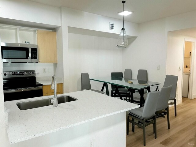 kitchen with visible vents, a sink, stainless steel microwave, light wood finished floors, and black range with electric stovetop