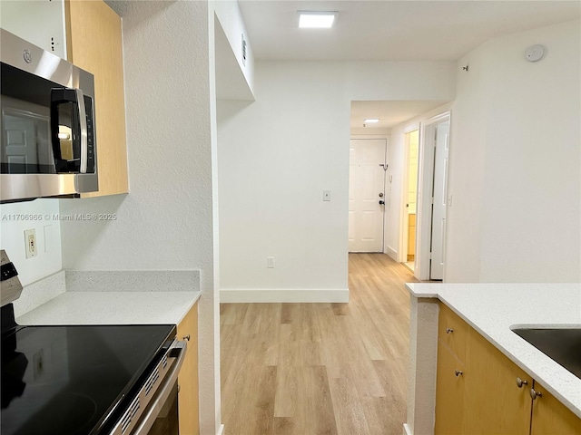 kitchen featuring baseboards, a sink, appliances with stainless steel finishes, light wood-style floors, and light stone countertops