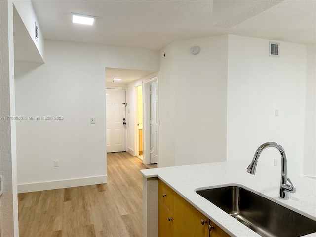 kitchen featuring baseboards, light wood-type flooring, light stone countertops, visible vents, and a sink