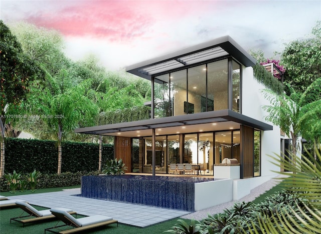 back house at dusk featuring a patio and a sunroom