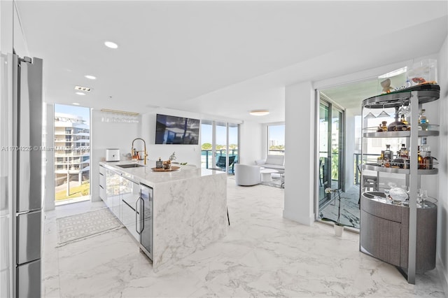 kitchen featuring white cabinets, stainless steel fridge, a wall of windows, and sink