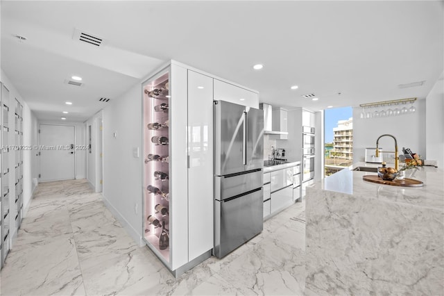 kitchen featuring light stone counters, stainless steel appliances, sink, wall chimney range hood, and white cabinets