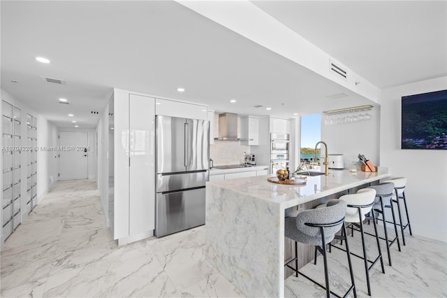 kitchen with white cabinets, wall chimney range hood, sink, a kitchen bar, and stainless steel appliances