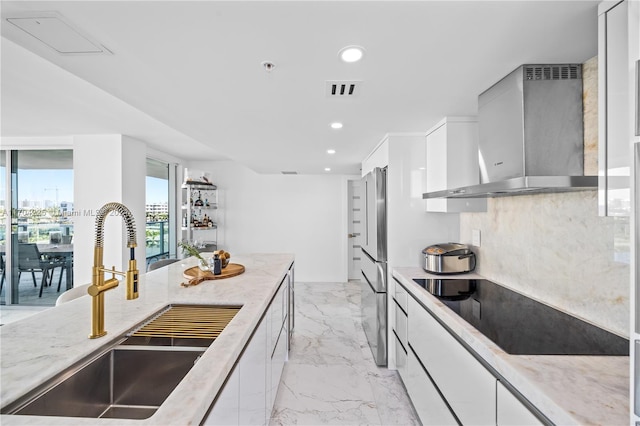 kitchen featuring light stone countertops, high end refrigerator, wall chimney exhaust hood, sink, and white cabinetry