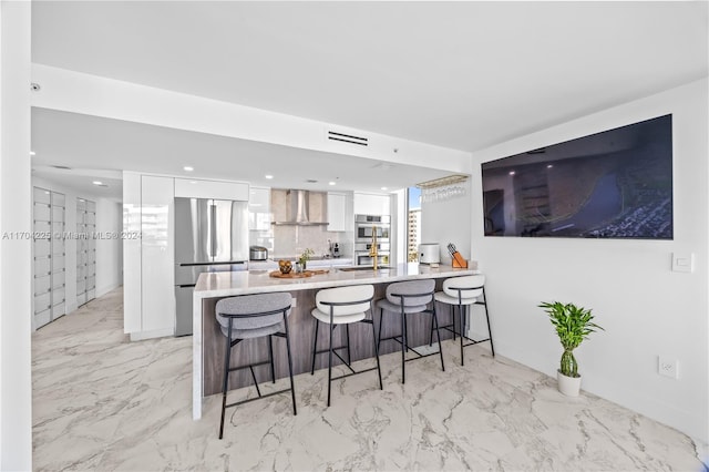 kitchen with a breakfast bar, stainless steel appliances, white cabinetry, and wall chimney range hood