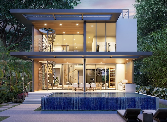 back house at dusk with a balcony, a patio, and an outdoor kitchen