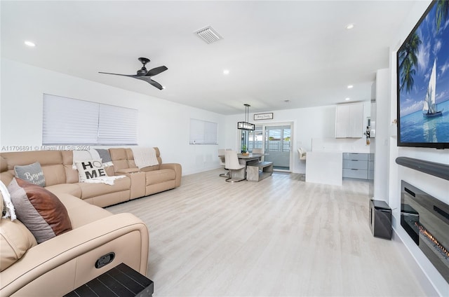 living room featuring ceiling fan with notable chandelier and light hardwood / wood-style floors